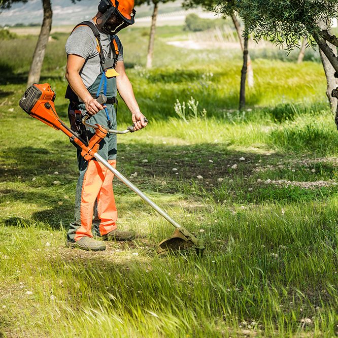 a,man,wearing,helmet,and,protective,clothing,while,trimming,grass